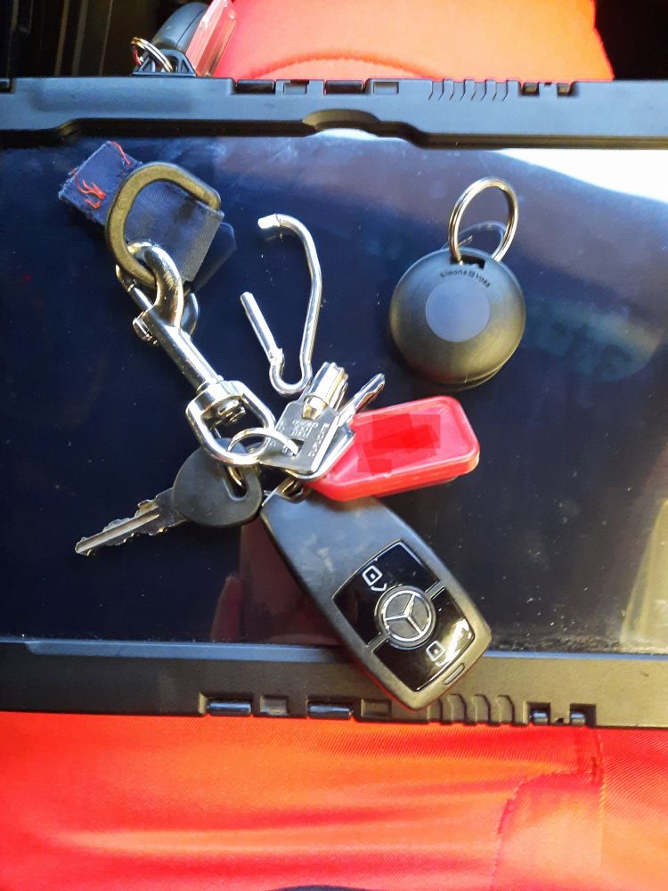 Ein Schlüsselbund liegt auf einem Tablet. Der Schlüsselbund hängt an einem Ring, der an einem abgerissenen Stofffetzen befestigt ist. Daneben ist ein verbogener Karabiner und ein einzelner Transponder.