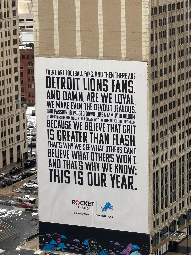 Poster on the side of a building in Detroit with the fllllwing text:

There are football fans and then there are Detroit Lions fans. And damn, are we loyal. We make even the devout jealous. Our passion is passed down like a family heirloom. Generations of Honolulu Blue collars with white-knuckle optimism. Because we believe that grit is greater than flash. That’s why we see what others can’t. Believe what others won’t. And that’s why we know: this is our year. 