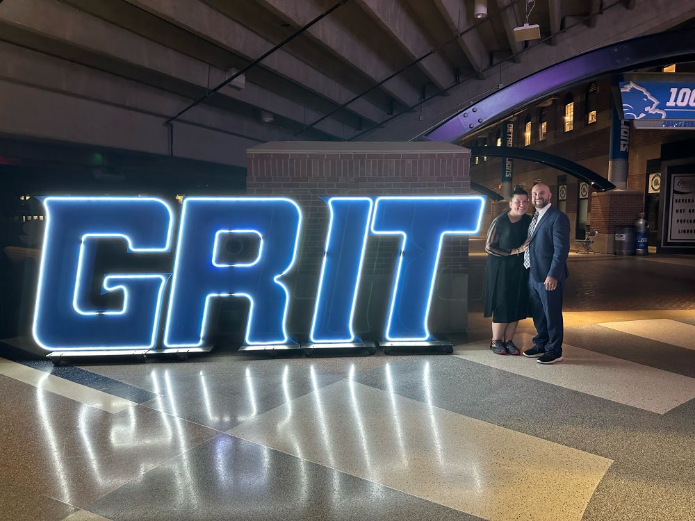 Two people next to a neon sign: “GRIT” at Ford Field