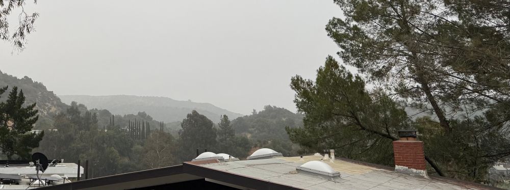 Rooftops, trees & distant hills under an overcast sky
