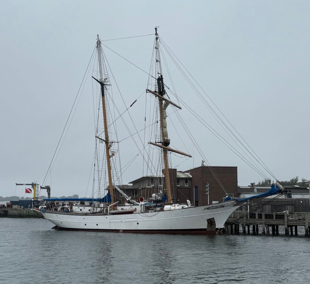Two masted 134 foot sailing ship at a dock with buildings in the background 