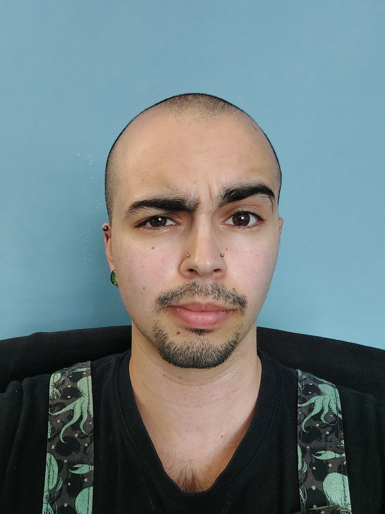 A selfie of Umbreon. They have a shaved head and a goatee. They are raising one eyebrow. 