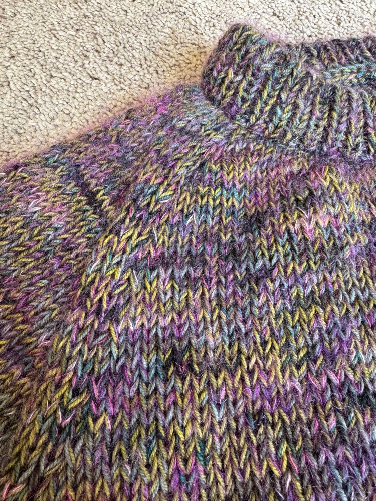 A close up view of the right front shoulder of the purple, green, and blue marled sweater showing the halo from the mohair strand of yarn.