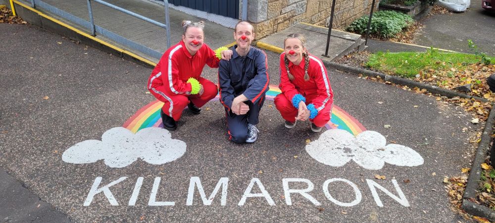 Characters Dot, Dash and Minum crouching down next to a painting on the floor that says Kilmaron with a rainbow round it