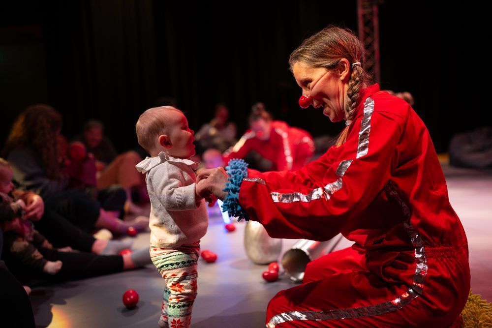 Photo from production Laaaunch! of artist Fiona holding hands with a small baby who is standing