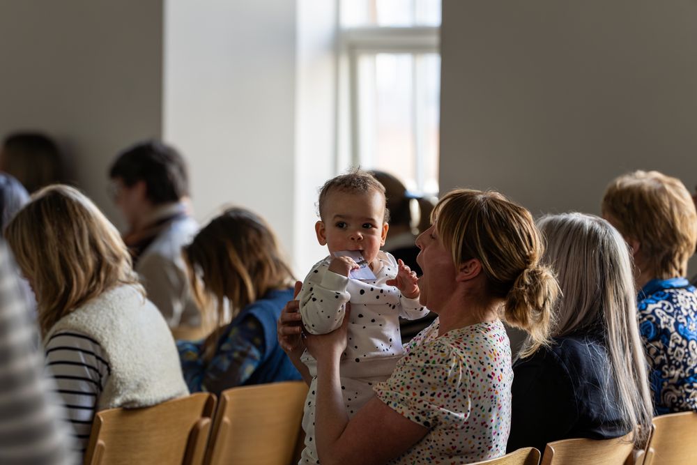 Photo from The Right Start conference. An adult holding up baby sitting amongst a crowd of people