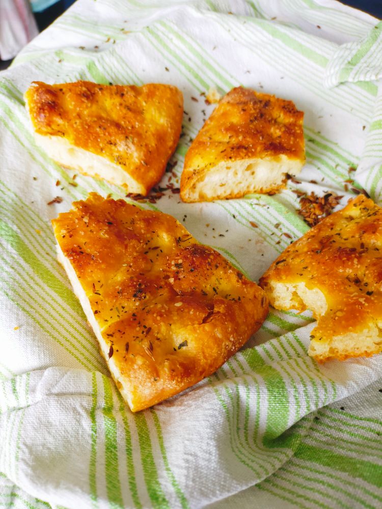 De la focaccia en petites parts, bien dorée, posée sur un torchon blanc à rayures vertes