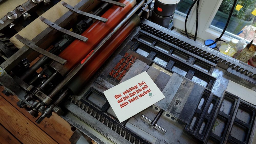 Druck in Bleisatz mit dem in roter Fraktur ausgeführten Text Wer unbedingt stolz auf sein Volk sein will sollte Imker werden. Neben der Bleisatzform auf der Druckmaschine