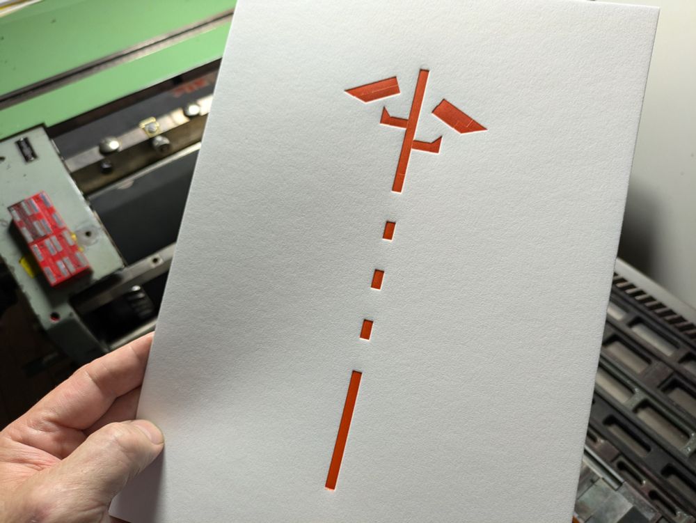 Foto meiner Hand, die den Rot-Abzug vor die Druckmaschine hält.
