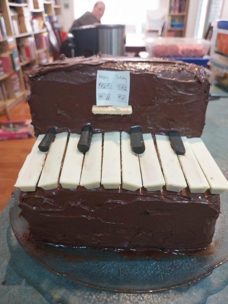 A cake in the shape of a piano, with white and black keys and a little song book