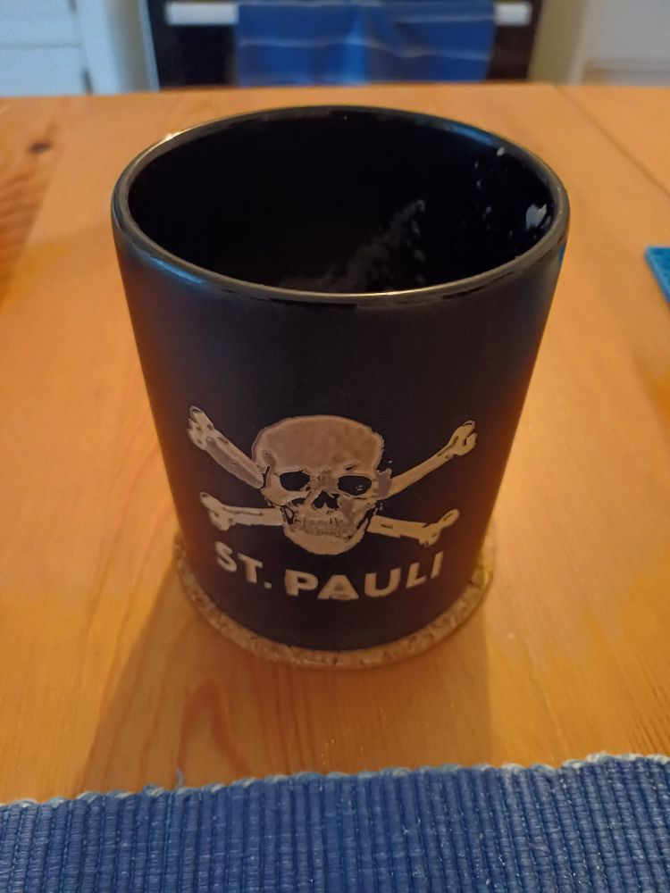 Schwarzer Kaffeebecher mit St. Pauli-Emblem.