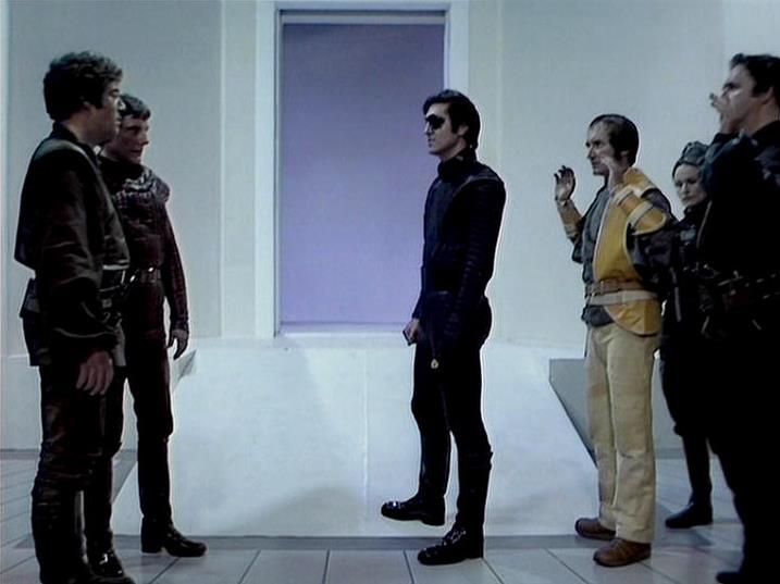 

Claude Sonnet 4.0 describes the image as: "This appears to be a scene from a science fiction television series set in a sterile, white-walled futuristic environment. Several characters are gathered in what looks like a spaceship or space station corridor, with a doorway or window showing a purple/violet glow in the background. The characters are wearing various costumes typical of 1970s/80s sci-fi productions - including dark leather or fabric outfits and more casual clothing. The setting and costumes suggest this is from a dramatic scene, possibly involving tension or confrontation between the characters. The stark, minimalist set design with clean lines and bright lighting creates a distinctly futuristic atmosphere typical of British science fiction television of that era."

Blakes7Bot, version 3.9.31. AWS Lambda version: 1.14.