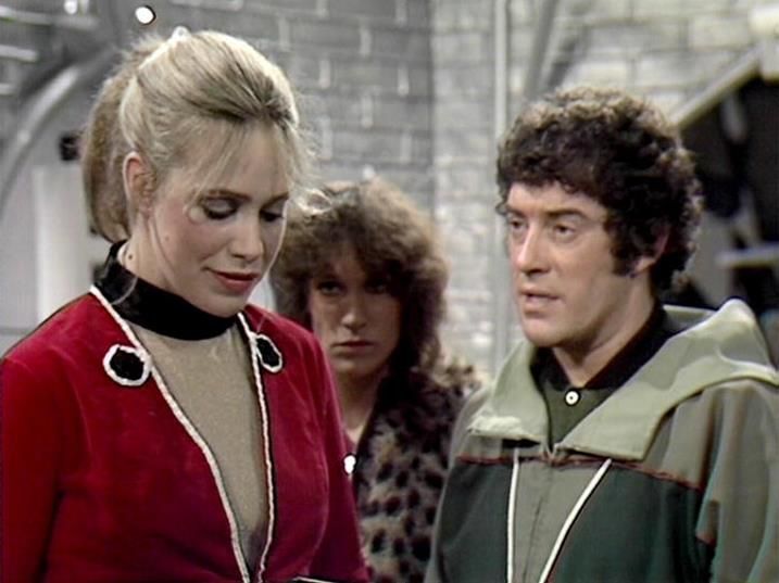 

Claude Sonnet 4.0 describes the image as: "This image appears to be from a classic British science fiction television series, likely from the late 1970s or early 1980s based on the production quality and costume design. The scene shows three characters in what appears to be a spaceship or futuristic facility interior, with industrial gray walls visible in the background.

The woman on the left wears a distinctive red velvet tunic with white cord trim and a black turtleneck underneath, styled with blonde hair pulled back. Her costume suggests a character of some authority or importance. The middle figure has curly dark hair and wears a patterned top, while the person on the right is dressed in a green and beige uniform with shoulder detailing, suggesting a military or crew member role.

The setting has the characteristic look of BBC science fiction productions from this era, with practical sets and functional costume designs"

Blakes7Bot, version 4.0.1. AWS Lambda version: 1.14.