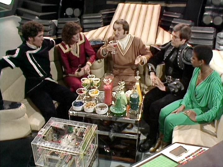 

Claude Sonnet 4.0 describes the image as: "This scene shows the crew gathered in what appears to be a luxurious lounge area aboard their ship. The setting features comfortable seating arranged around an elegant glass coffee table laden with refreshments including drinks, snacks, and what looks like tea service. The space has a sophisticated, almost decadent atmosphere with rich furnishings and warm lighting.

The crew members are dressed in their typical attire - some in leather jackets and others in flowing robes or tunics. They appear to be having a social moment, relaxing together in this opulent setting. The contrast between their usual serious missions and this comfortable, almost hedonistic environment creates an interesting dynamic. The scene suggests a rare moment of leisure and camaraderie among the group."

Blakes7Bot, version 3.9.31. AWS Lambda version: 1.14.