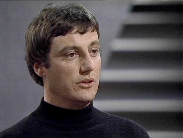 

Claude 3.7 describes the image as: "The image shows a person in what appears to be a scene from a television production, likely from the late 1970s or early 1980s based on the visual style and quality. They are wearing a black turtleneck sweater and have short dark hair. The background is minimalist and gray, with what looks like stairs or stepped architecture visible behind them.

The lighting and cinematography have that distinctive quality common in British sci-fi television productions of that era - somewhat stark and theatrical. The person has a thoughtful or serious expression, captured in what seems to be a dramatic moment. The composition and styling suggests this is from a science fiction series, with the simple costuming and set design typical of productions from that period."

Blakes7Bot, version 3.9.31. AWS Lambda version: 1.14.