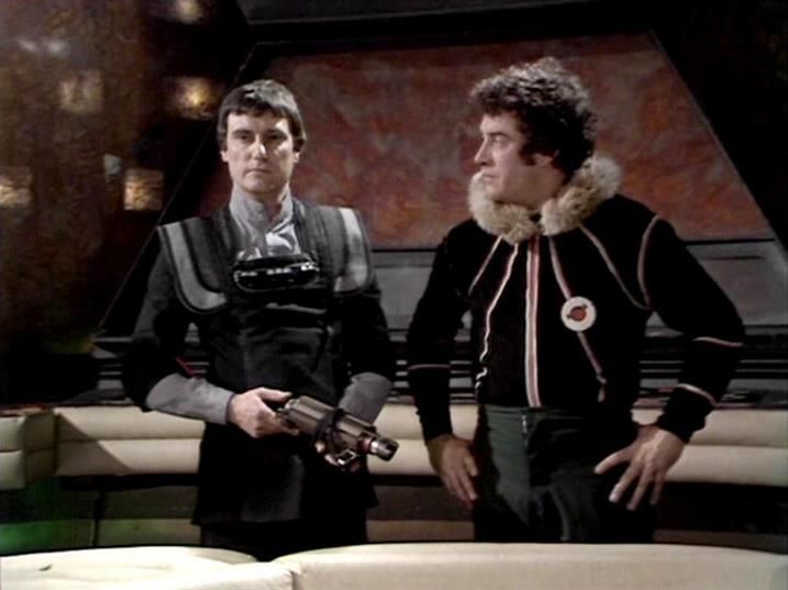 

Claude Sonnet 4.0 describes the image as: "This scene shows two characters in what appears to be the interior of a spacecraft, likely the Liberator. The setting has a distinctive futuristic design with curved walls and lighting typical of the show's aesthetic. One character wears dark leather-style clothing and holds what appears to be a weapon, while the other is dressed in a black outfit with fur trim around the collar. They appear to be having a conversation while seated on what looks like a bench or seating area within the ship's interior. The lighting and set design create the atmospheric, somewhat austere environment characteristic of the series' spacecraft settings."

Blakes7Bot, version 3.9.31. AWS Lambda version: 1.14.
