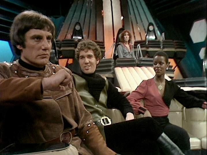 

Claude 3.7 describes the image as: "This image shows a scene from a sci-fi television series set in what appears to be a spacecraft control room or command center. The futuristic set features distinctive ribbed wall panels and technical equipment typical of 1970s/80s British television science fiction production design.

Four performers are shown in the spacecraft interior, seated in what looks like a command area. One person wearing a brown leather-like outfit with buckles sits prominently in the foreground, while others are positioned around what appears to be a control console. The styling and costumes reflect the aesthetic of classic British science fiction television, with practical set design and character-specific wardrobe choices.

The image has the characteristic look of television production from that era, with studio lighting and set construction typical of BBC productions of the time."

Blakes7Bot, version 3.9.31. AWS Lambda version: 1.14.