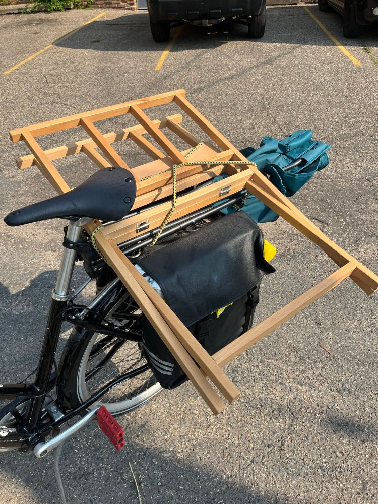 A bicycle rear rack with an art rack and camp chair tied on top of a pannier