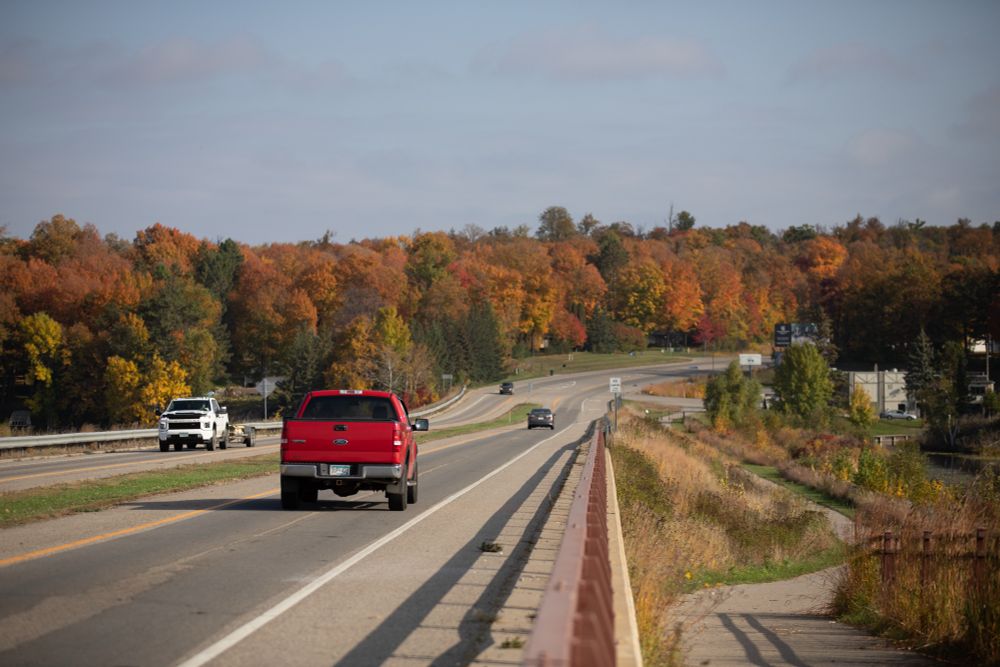 A red truck drives north on Hwy 169 with autumn color trees in the background
