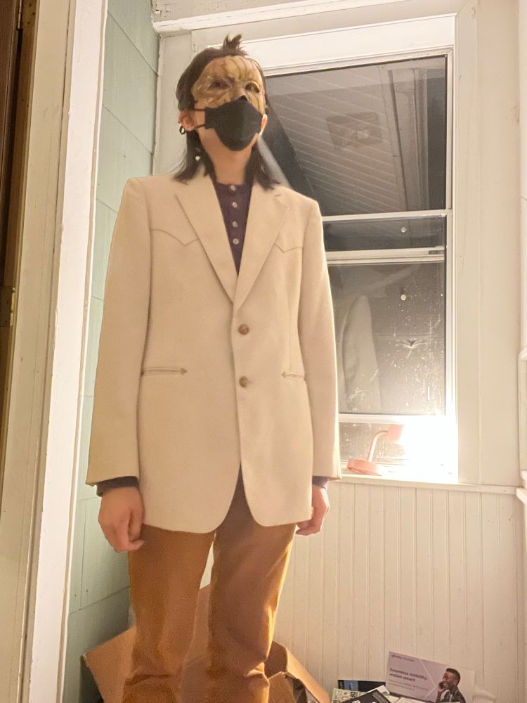 A person dressed in a white blazer wearing a masquerade mask