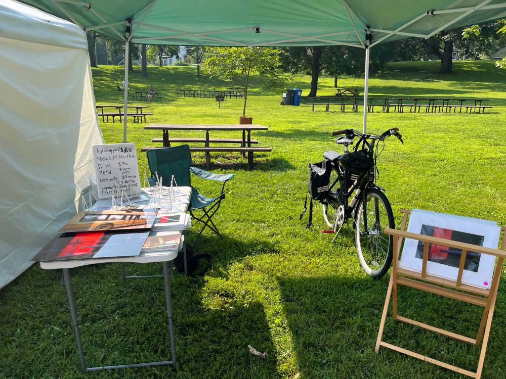 A booth with photographs, bike, and a sign that says to “mask up.”