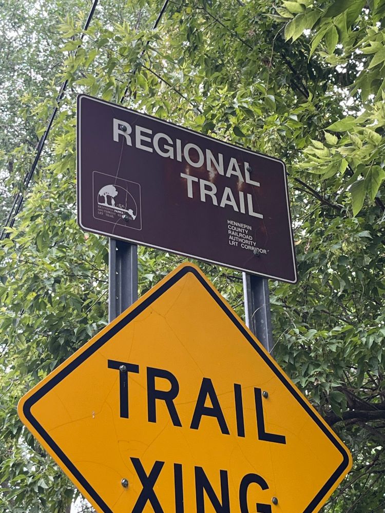 An old Hennepin County regional trail sign mounted on top of a Trail Xing sign