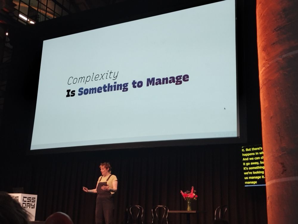 Miriam standing on stage before a slide that says "complexity is something to manage"