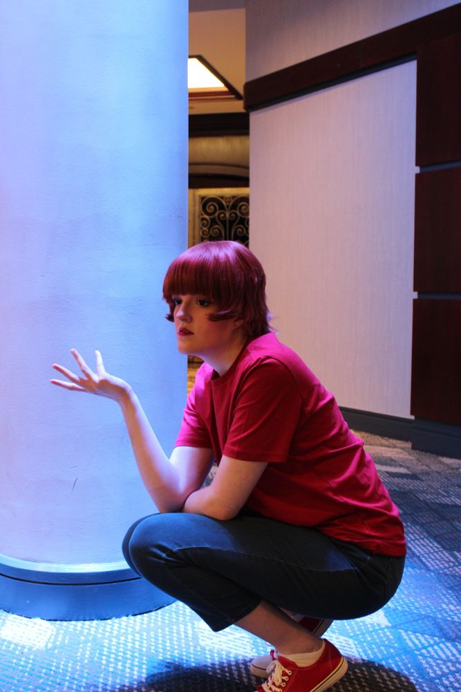 The same person crouching by the pillar, now with their hand held out instead of supporting their head.