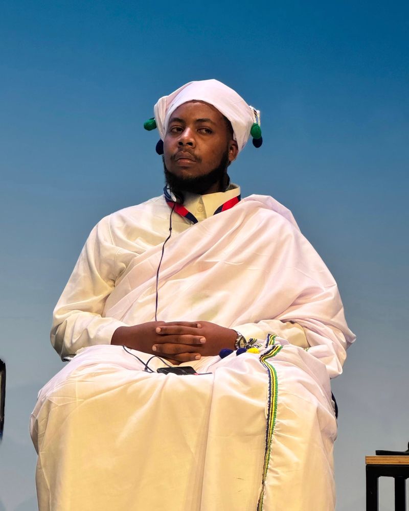A man in a white traditional garment, sitting. 