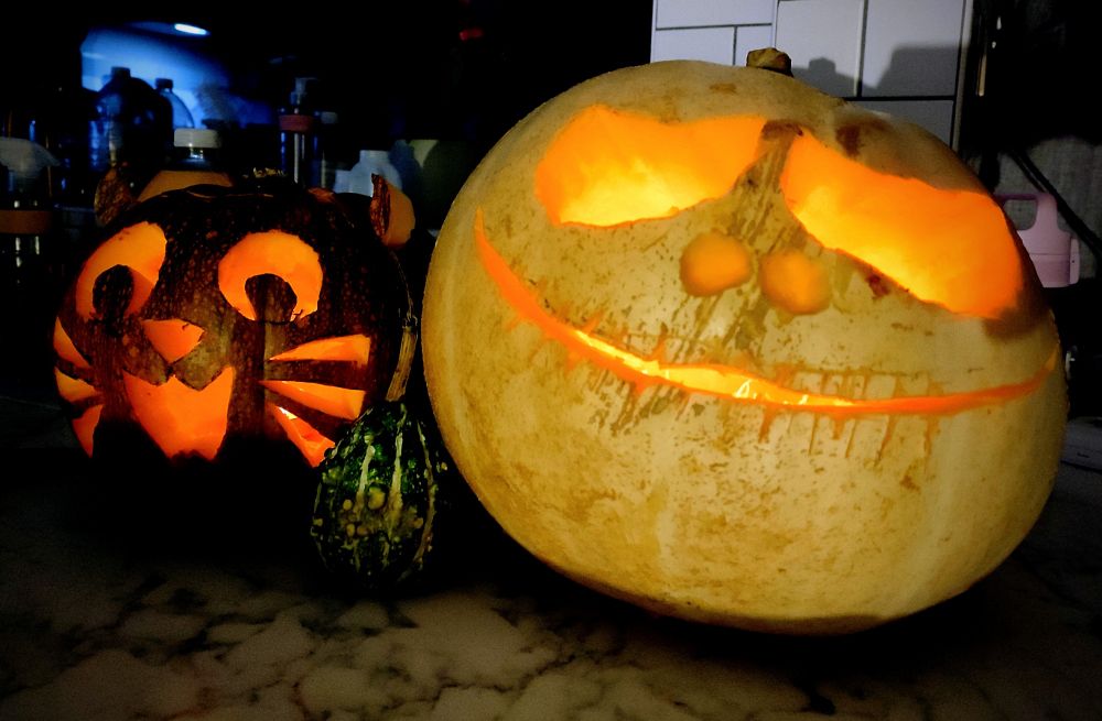 A medium sized orange pumpkin carved like a cat and a big white pumpkin carved like Jack Skellington 