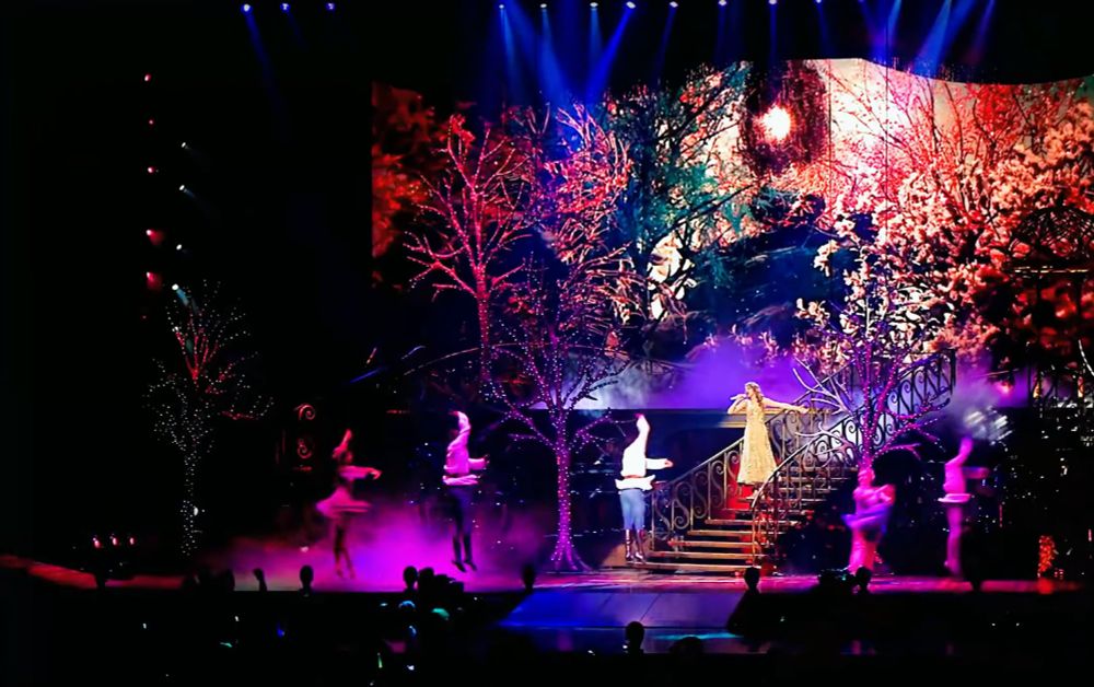 wide shot of the beginning of enchanted at the speak now world tour. several dancers are on stage as taylor swift descends the staircase singing.