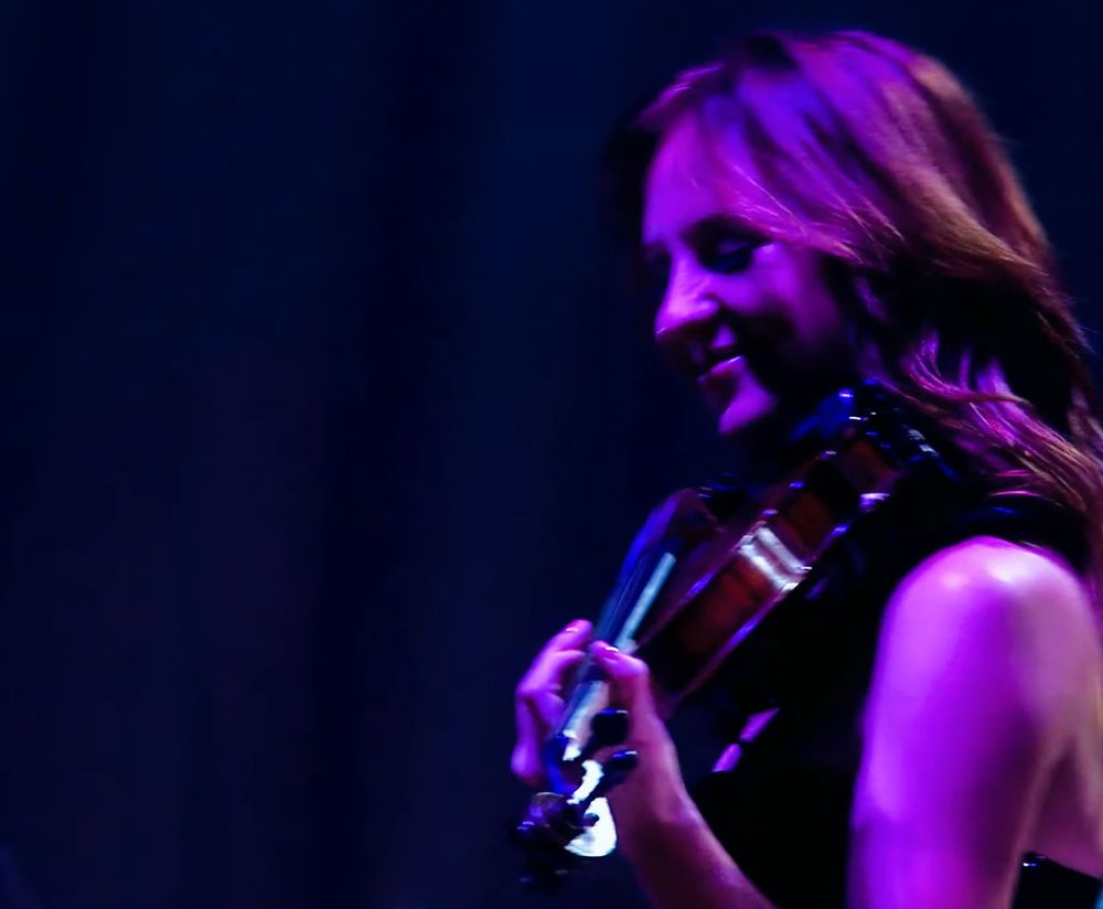 violinist caitlin evanson smiling as she plays her violin during the instrumental intro for enchanted at the speak now world tour