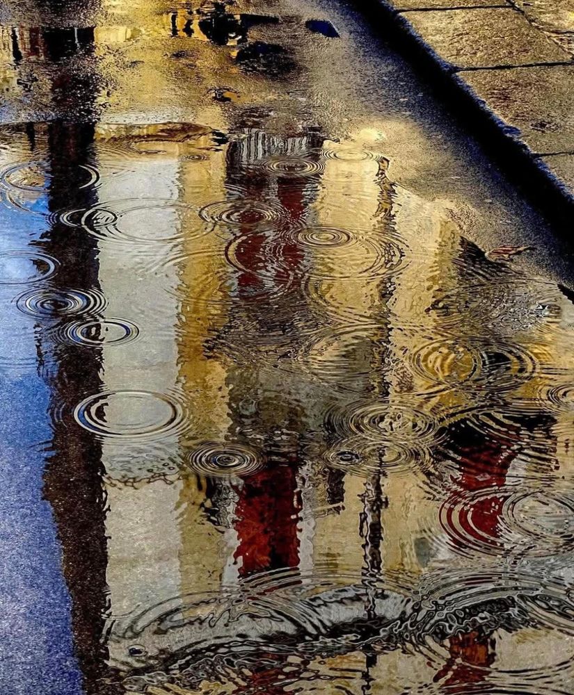 Photographie d'une flaque sur le goudron au pied d'un trottoir, il pleut beaucoup.