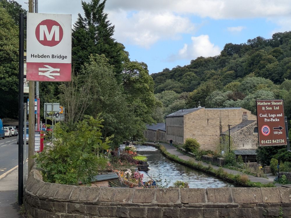 The station sign for Hebden Bridge with the Hebden Canal in the background 