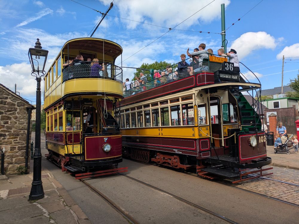 Two vintage trams parked side by side in a sunny heritage street