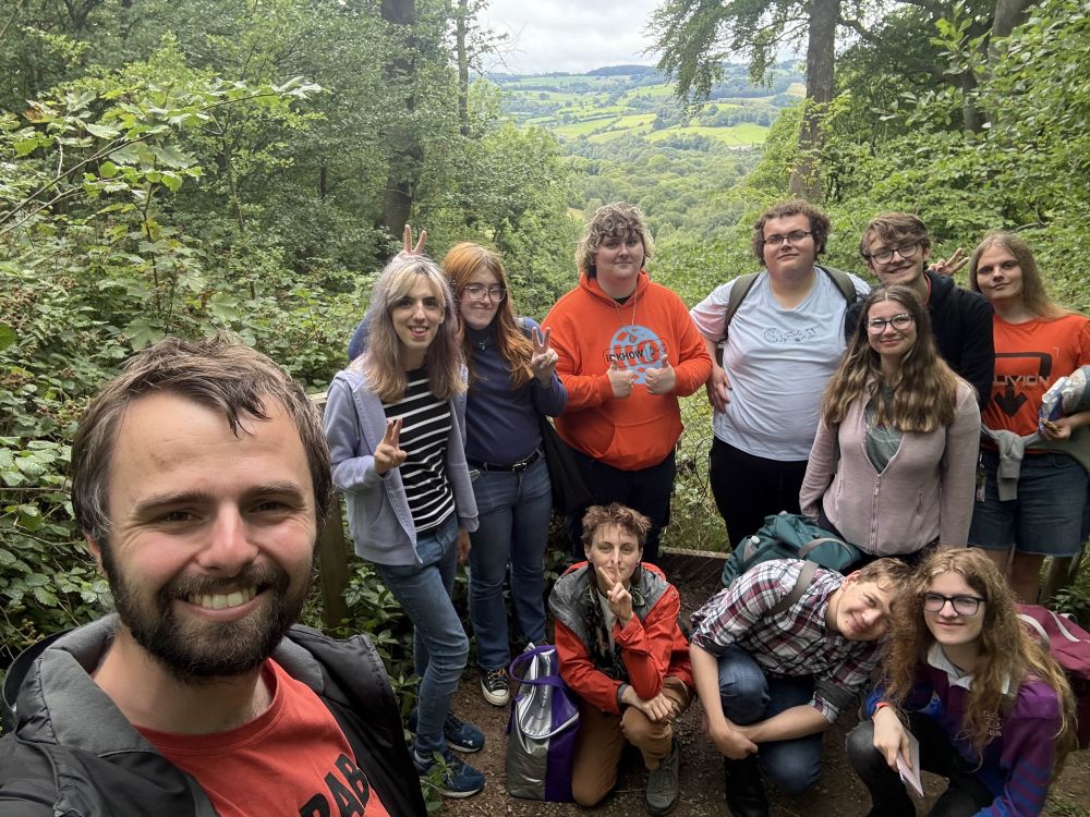 A group of 11 friends smiling at the camera with green leaves and hills in the background 