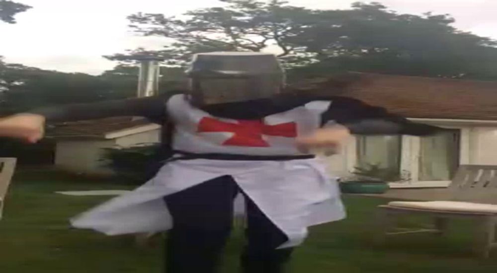 a man dressed as a knight with a cross on his chest is dancing in a yard .