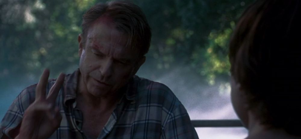 Screenshot of Jurassic Park 3. A disheveled and bloody Sam Neill holds up two of his fingers.