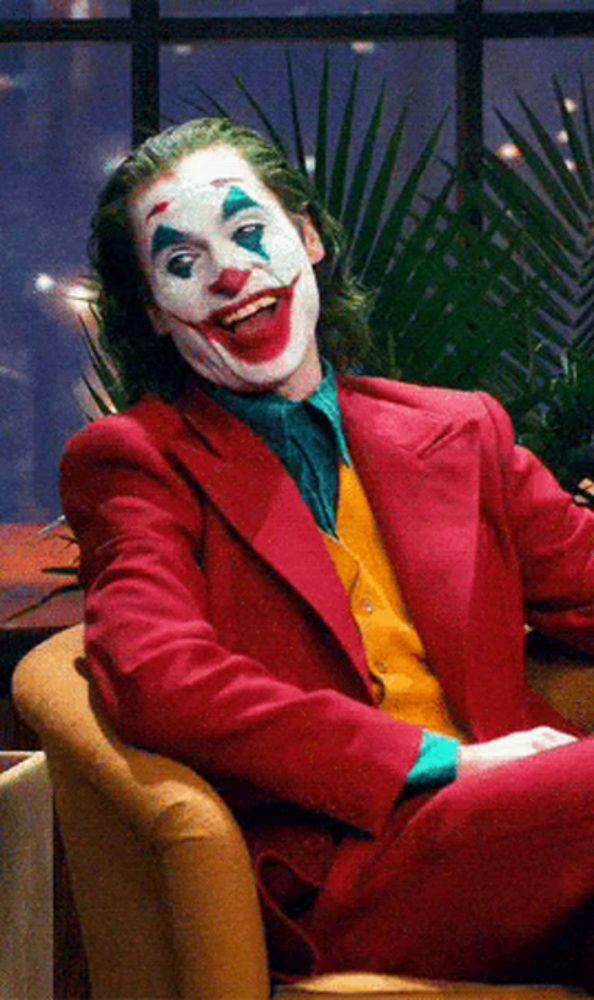 the joker is sitting in a chair with his mouth open