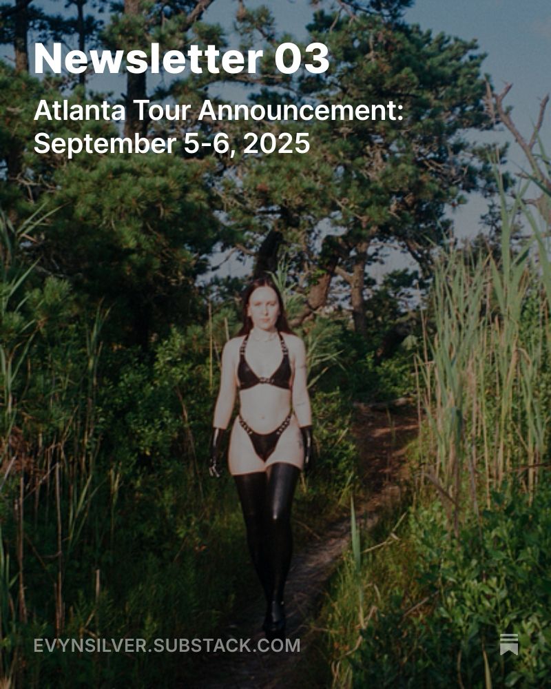 Evyn Silver, a white femme with long dark hair, walks along a sunny path between conifer trees, bare branches, and beach grass. She wears a silver chain necklace, a black latex set with buckles, black latex gloves, black latex stockings, and shiny black platform heels. White text reads: “Newsletter 03, Atlanta Tour Announcement: September 5-6, 2025, evynsilver.substack.com.”