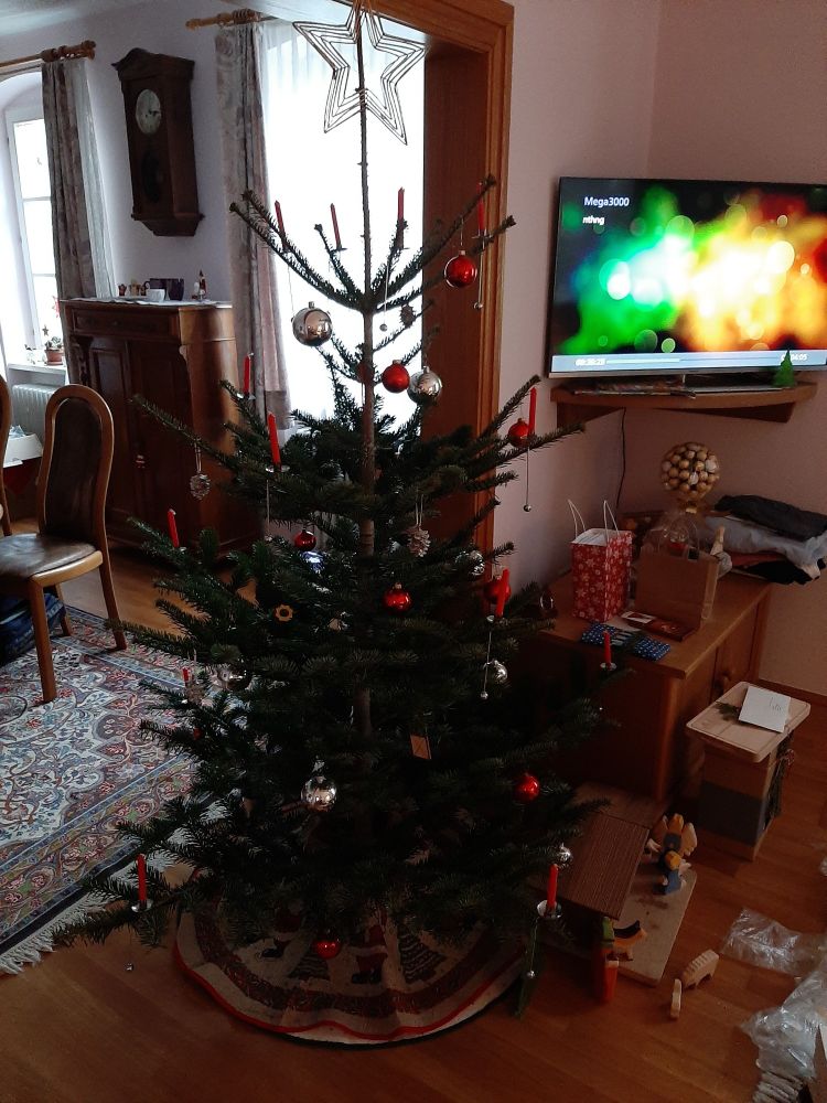 Ein (teilweise) geschmückter Weihmachtsbaum steht in einem Wohnzimmer