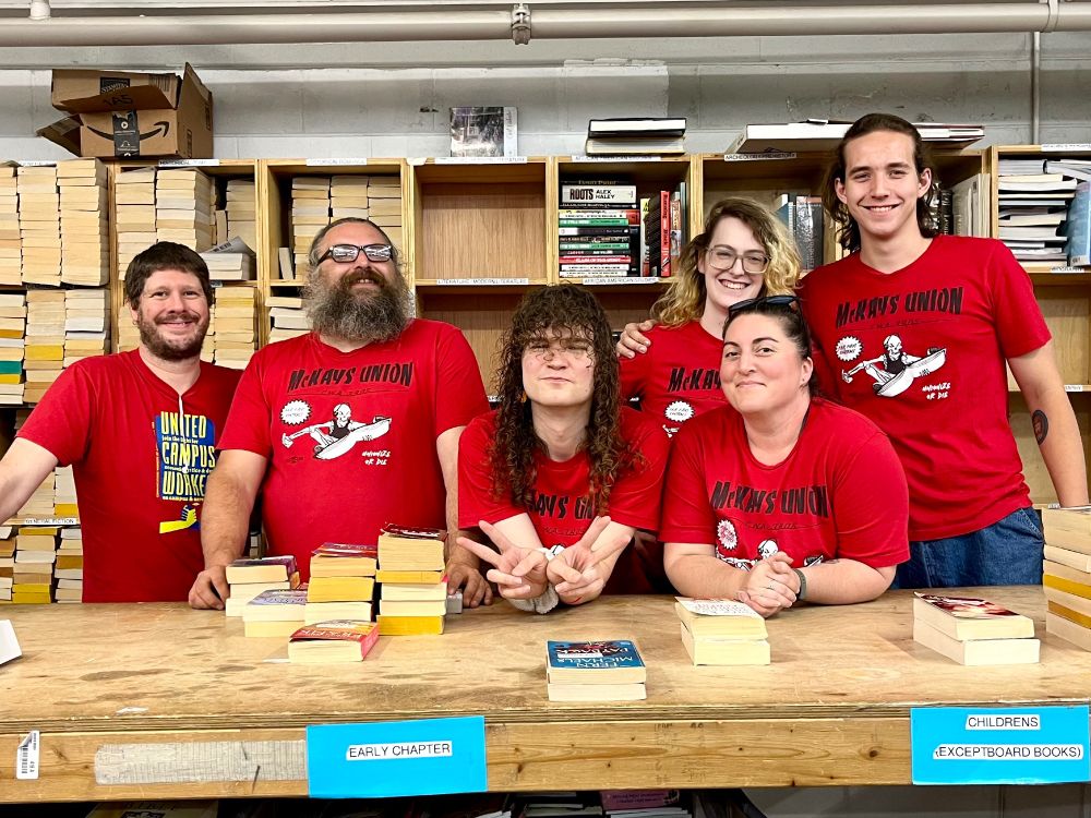 Five coworkers stand behind a table, all wearing red shirts. 