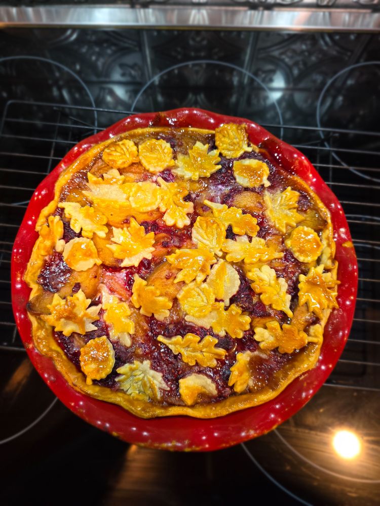 A peach raspberry pie with crust leaf cutouts in a red baking dish
