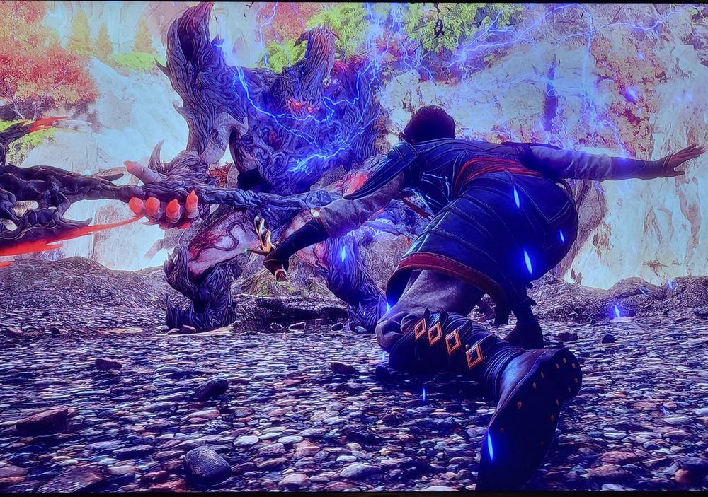 A screenshot from the game Dragon Age Veilguard. The camera is positioned behind the player character Rook, who is crouched with a dagger in their left hand and shooting lightning from their right hand at a huge demon monster that is at least twice as big as them