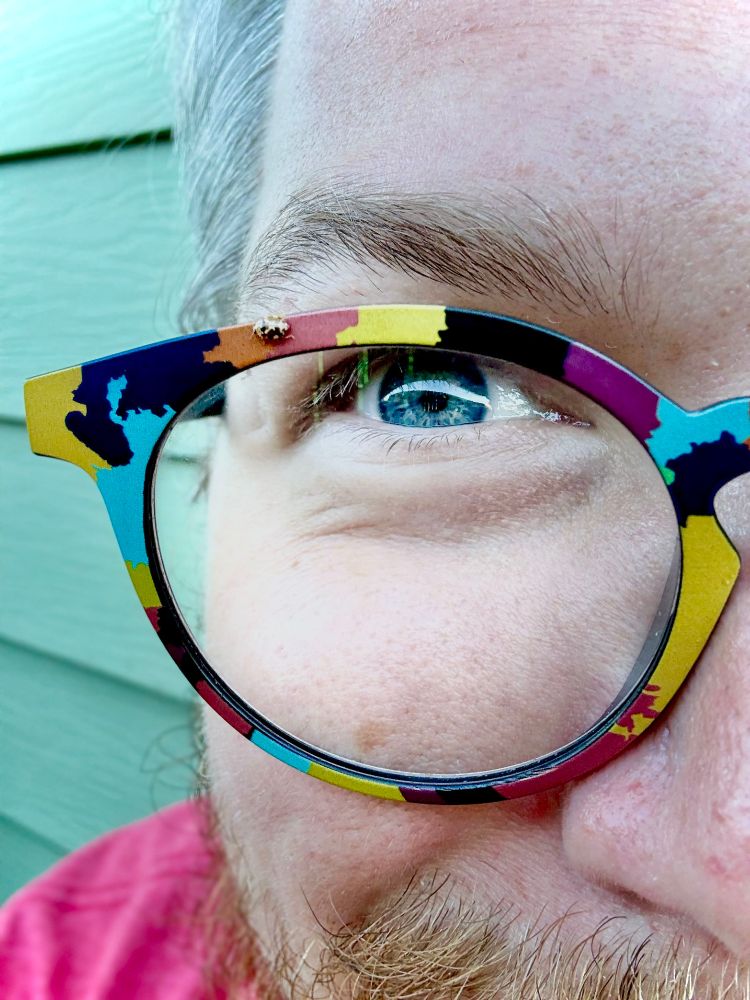 very very close up, overly vibrant picture of a happy lil guy wearing a pair of colorful glasses with a tiny ladybug on them.