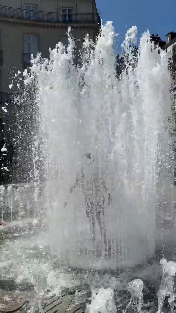 Within a cascade of water shooting from a floor level fountain is the silhouette of a girl 
