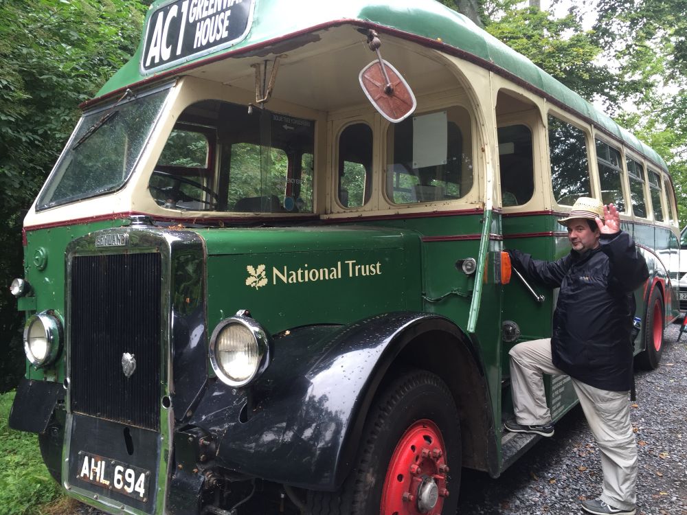 A big old green bus with red wheels. A man in a hat is waving at the camera while pretending to board. 
Apparently ‘The Greenway Estates' bus (A Baranaby-bodied Leyland Tiger PS1 registered AHL964) […] used to take visitors to and from Agahta Christie's old house which is now managed by the National Trust’ - Wikimedia https://commons.wikimedia.org/wiki/File:Galmpton_-_Greenway_bus_AHL694.jpg