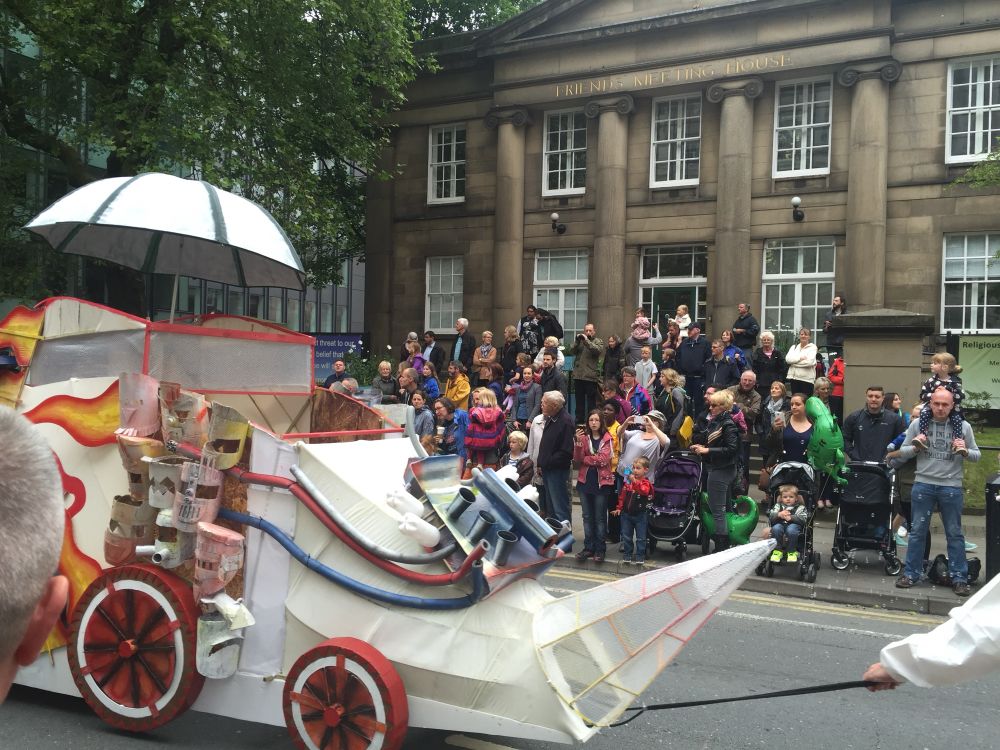 Fantasy vehicle on white with painted flames in red and yellow from red and white wheels. It’s a float being pulled as part of the parade