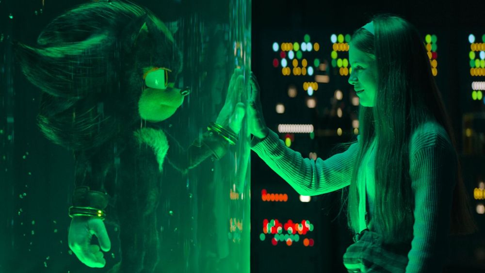 Shadow and Maria placing their hands together through the glass.