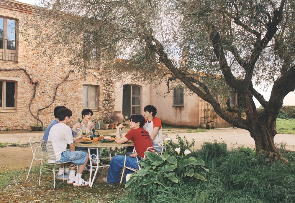 Five Asian men [members of Tomorrow x Together TXT] sitting on a table at a backyard of a farmhouse